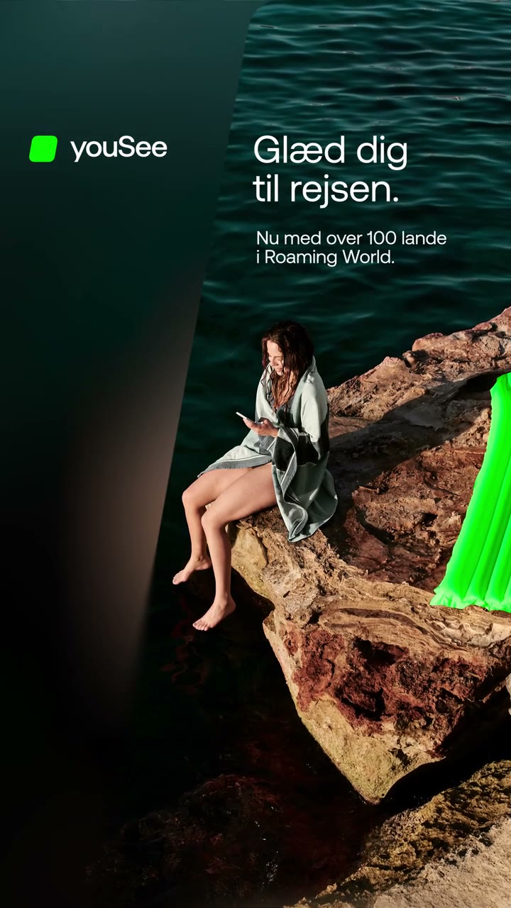 Vertical YouSee ad: a woman reads on sun-warmed rocks by dark green water, a bright green inflatable at the edge of frame, as "Glæd dig til rejsen" fades in beside the YouSee logo before a blur transition to the end card.